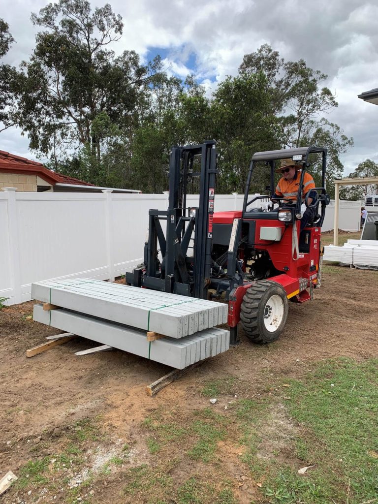 A worker operating a red forklift moving bundled concrete posts at a construction site A worker operating a red forklift moving bundled concrete posts at a construction site