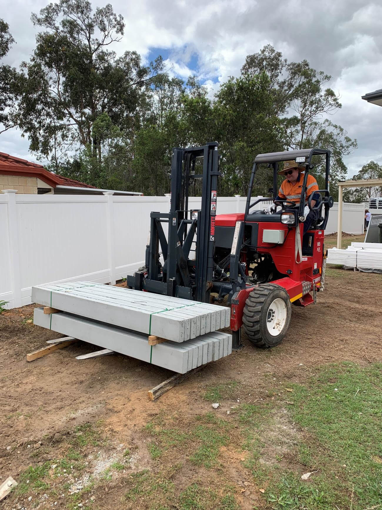 A worker operating a red forklift moving bundled concrete posts at a construction site