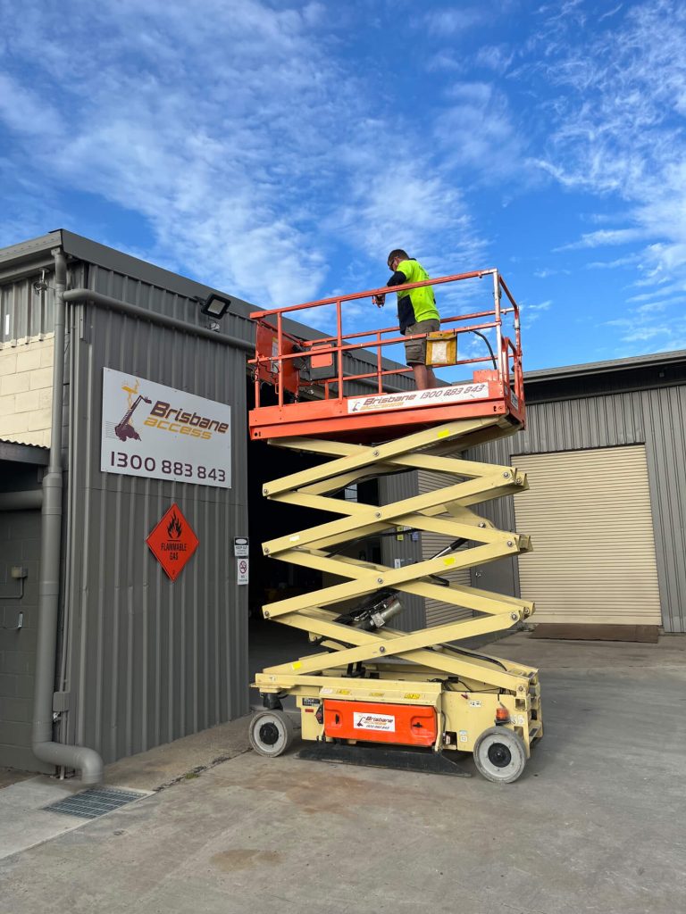 A worker in high-vis clothing standing on an elevated scissor lift performing maintenance on a building exterior A worker in high-vis clothing standing on an elevated scissor lift performing maintenance on a building exterior