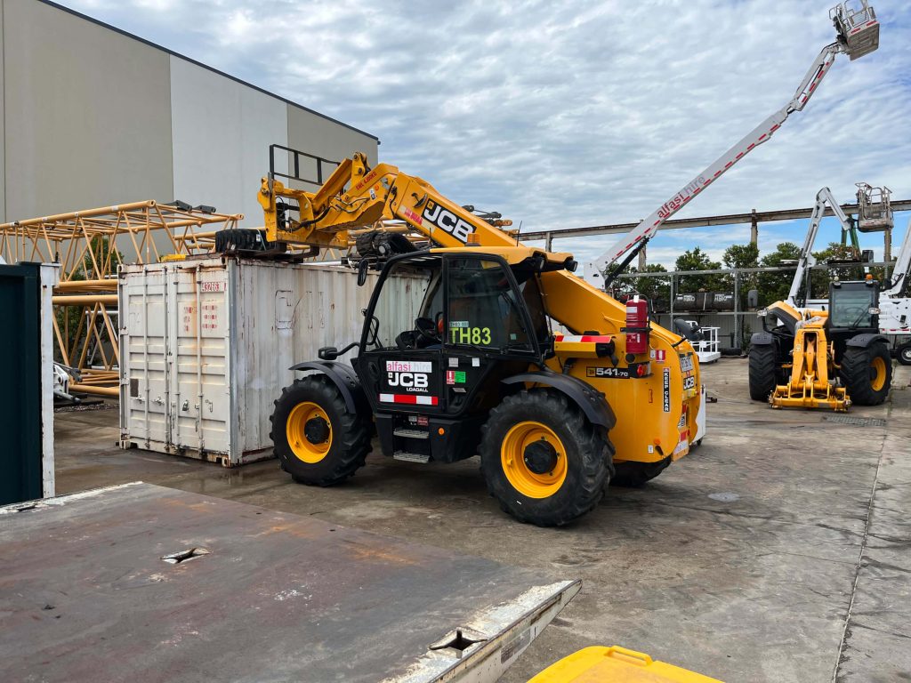 A JCB telehandler lifting equipment onto a shipping container at a construction site A JCB telehandler lifting equipment onto a shipping container at a construction site