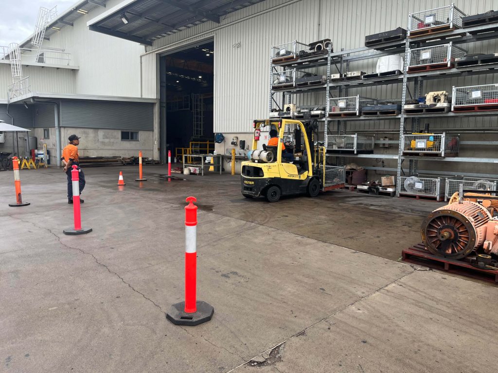 A worker operating a yellow forklift truck near a warehouse entrance, manoeuvring through safety cones - Licence to operate a forklift truck A worker operating a yellow forklift truck near a warehouse entrance, manoeuvring through safety cones - Licence to operate a forklift truck