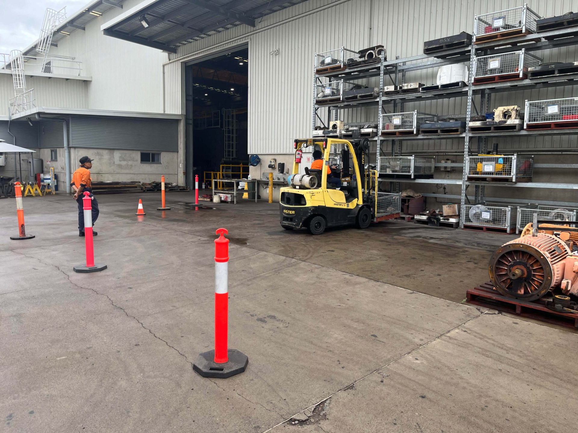 A worker operating a yellow forklift truck near a warehouse entrance, manoeuvring through safety cones - Licence to operate a forklift truck
