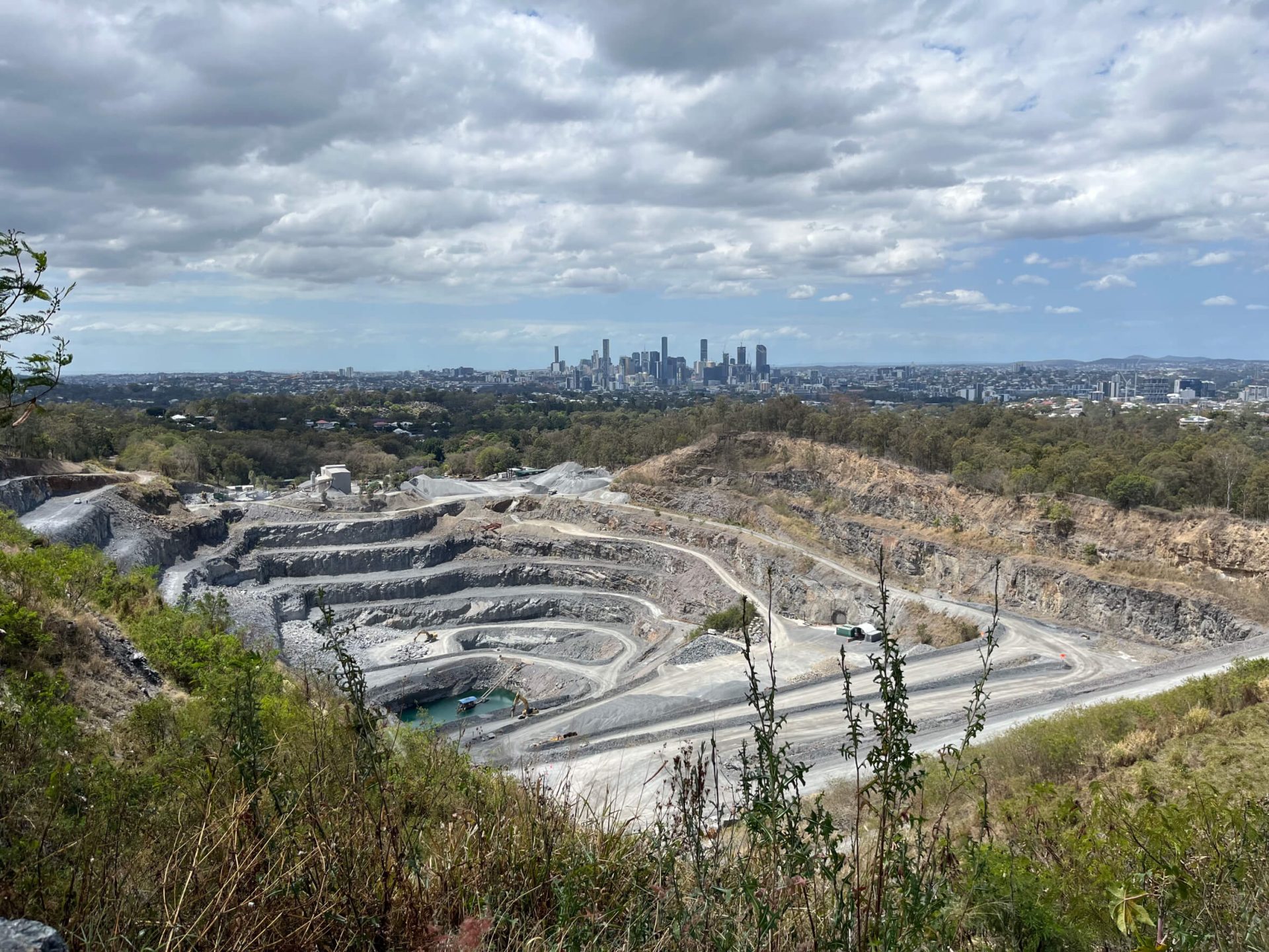 A view of a quarry site with a distant skyline in the background, showing urban development near an extraction site