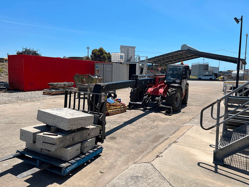 A telehandler carrying large concrete blocks at an industrial site, highlighting material handling and site operations A telehandler carrying large concrete blocks at an industrial site, highlighting material handling and site operations